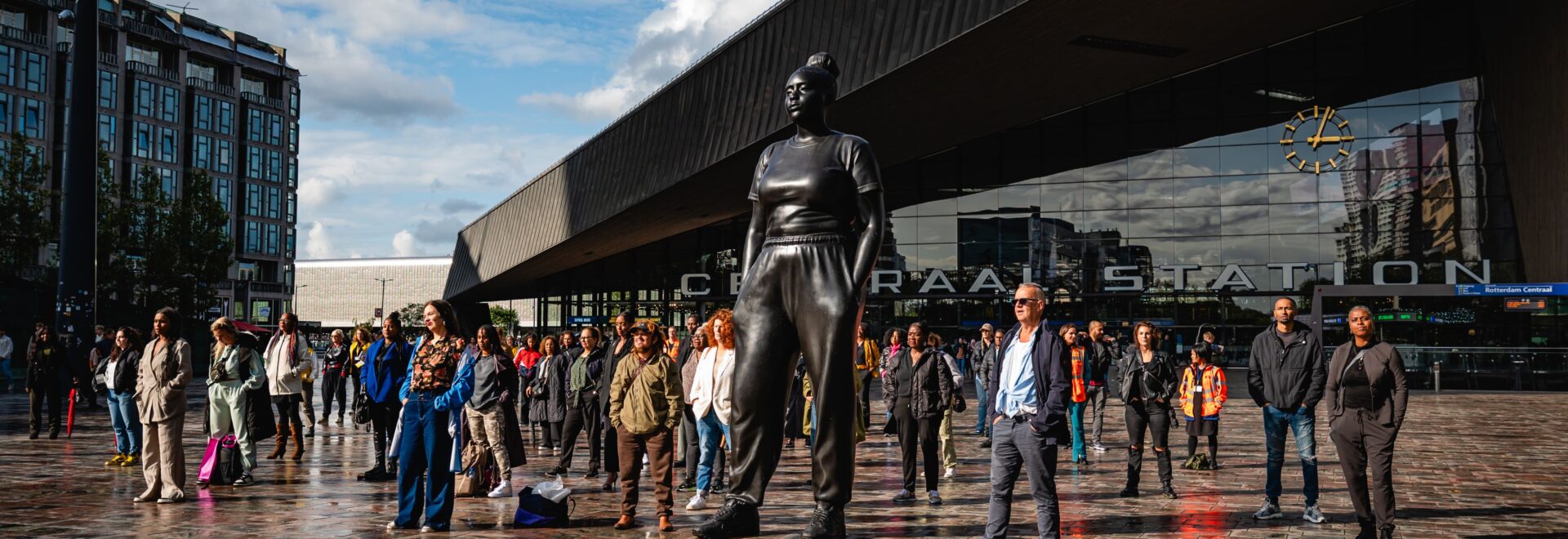 Foto van het plein van Centraal Station Rotterdam met op de voorgrond het beeld 'Moments Contained' met bezoekers van het station in dezelfde houding. Foto gemaakt in het kader van Diversity Day 2023 door Michelle Urbiztondo.