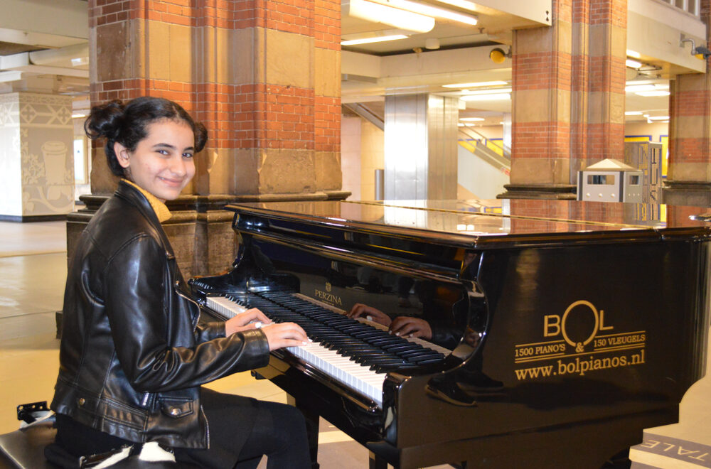Een jongedame bespeelt de piano op Amsterdam Centraal